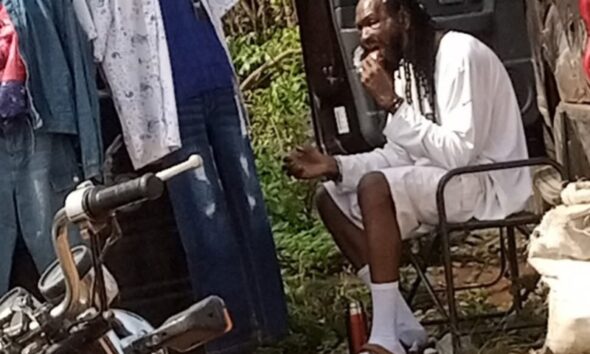 Outrage As Man Shares Photo Of Actor Sylvester Madu Selling Clothes And Eating On Bushy Road