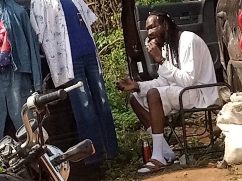 Outrage As Man Shares Photo Of Actor Sylvester Madu Selling Clothes And Eating On Bushy Road